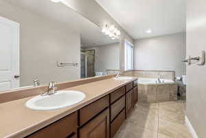 Full bathroom featuring double vanity, a shower stall, a garden tub, and light tile patterned floors