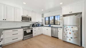 Kitchen with stainless steel appliances, white cabinets, light wood finished floors, and recessed lighting