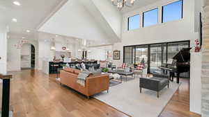 Living room with light wood-style flooring, suspended lighting, arched walkways, and a high ceiling