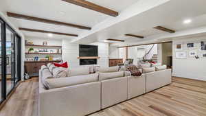 Living area with beam ceiling, light wood-style flooring, recessed lighting, a glass covered fireplace, and wooden walls