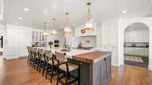 Dual tone kitchen featuring a kitchen breakfast bar, two tone cabinetry, a large island with sink, decorative backsplash, and light wood finished floors