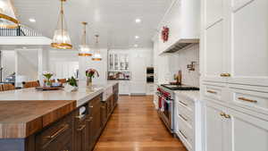 Kitchen with dual tone cabinetry, stainless steel appliances, decorative light fixtures, light wood-style flooring, and glass insert cabinets