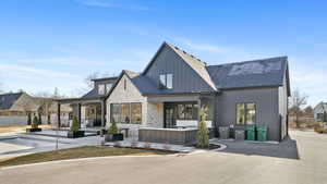 Rear view of property with a patio area, stone siding, board and batten siding, and roof with shingles