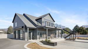 Rear view of house featuring a shingled roof, board and batten siding, asphalt driveway, a patio, and an attached garage