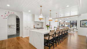 Kitchen with white cabinetry, a breakfast bar area, light wood-type flooring, light stone counters, and wooden ceiling