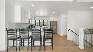 Kitchen with white cabinetry, stainless steel appliances, recessed lighting, light wood finished floors, and a peninsula