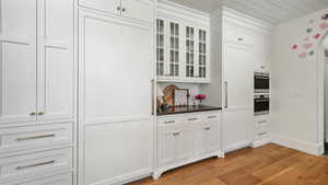 Kitchen featuring dark countertops, white cabinets, glass insert cabinets, light wood finished floors, and stainless steel double oven