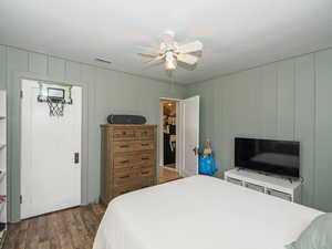 Bedroom featuring dark wood-style floors, ceiling fan, and wooden walls