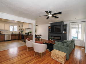 Living room with a ceiling fan, light wood-style flooring, crown molding, a large fireplace, and a textured ceiling