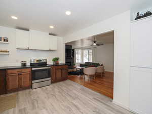 Kitchen with stainless steel range with electric cooktop, light wood finished floors, dark countertops, two tone color scheme, and a ceiling fan