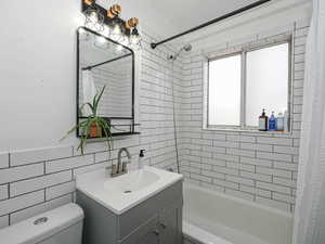 Full bathroom with tile walls, shower / bath combo with shower curtain, and vanity