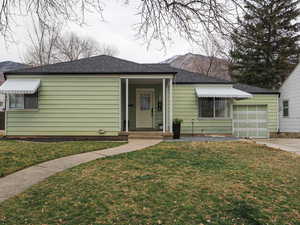 View of front of home with a front yard, roof with shingles, a garage, and driveway