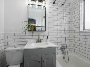 Bathroom with shower / bathtub combination, vanity, and tile walls