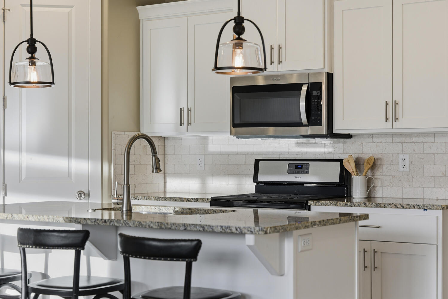 Kitchen with white cabinetry, stainless steel appliances, pendant lighting, and dark stone countertops