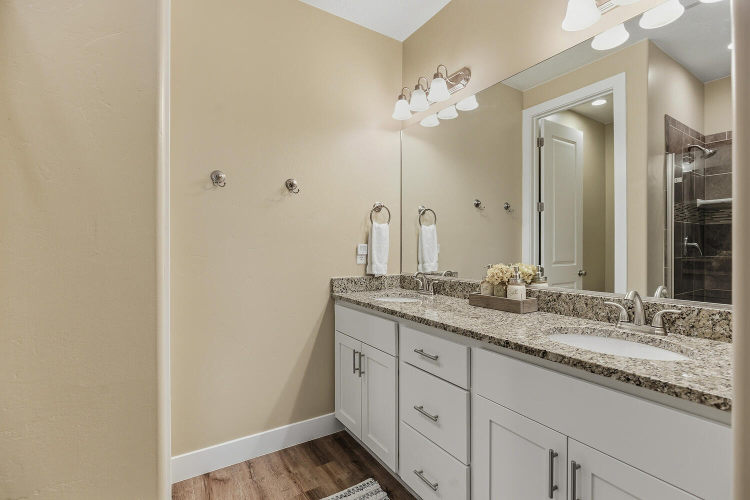 Full bath with double vanity, a stall shower, and light wood-style flooring