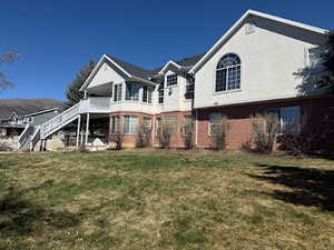 Rear view of property with a deck, brick siding, a yard, and stucco siding