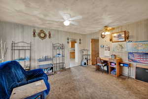 Office area featuring carpet floors, a ceiling fan, and wooden walls