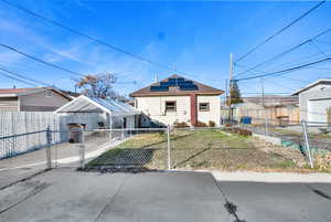 View of back of house featuring solar panels, a fenced front yard, and a gate