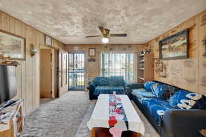 Living area with carpet flooring, ceiling fan, and wood walls