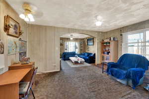 Living room featuring ceiling fan, arched walkways, carpet flooring, and wood walls