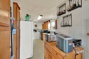 Kitchen featuring freestanding refrigerator, tile walls, gas range, light flooring, and a ceiling fan