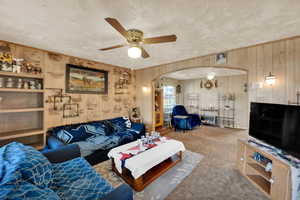 Living room featuring arched walkways, a ceiling fan, carpet, a textured ceiling, and wooden walls