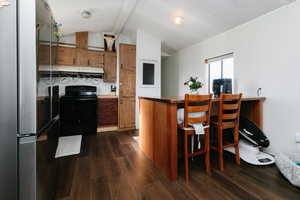 Kitchen featuring wood finish cabinetry, freestanding refrigerator, electric range, dark countertops, and a breakfast bar area
