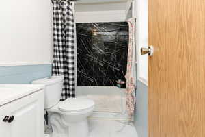 Bathroom featuring vanity, marble finish flooring, shower / tub combo with curtain, and a wainscoted wall