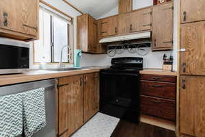 Kitchen with stainless steel appliances, light countertops, lofted ceiling, wood finish cabinetry, and dark wood-style floors