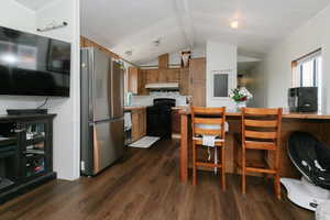 Kitchen featuring light countertops, freestanding refrigerator, wood finish cabinetry, black range with electric cooktop, and dark wood finished floors