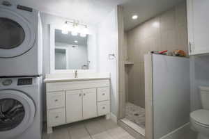 Full bath with vanity, walk in shower, recessed lighting, light tile patterned flooring, and stacked washing machine and dryer