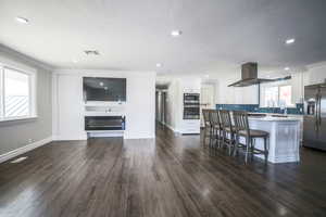 Kitchen featuring stainless steel appliances, white cabinets, a breakfast bar area, a kitchen island, and dark wood-style flooring