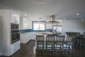 Main Kitchen featuring crown molding, stainless steel appliances, island exhaust hood, a kitchen island, and white cabinetry