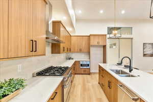 Kitchen featuring light stone counters, stainless steel appliances, light wood-style flooring, and pendant lighting