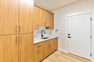 Laundry room with light wood finished floors,  a sink, and loads of storage.