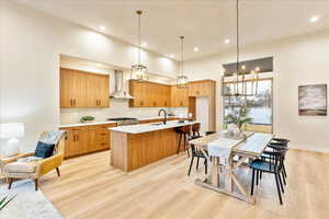 Kitchen with light wood-type flooring, tasteful backsplash, a kitchen island with sink, a kitchen bar, and suspended lighting