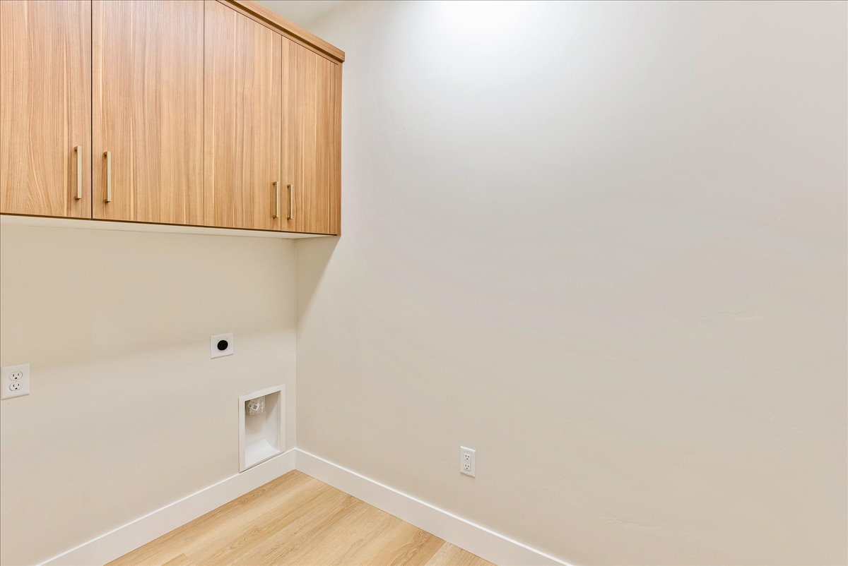 Laundry area with hookup for an electric dryer, cabinet space, and light wood-style flooring