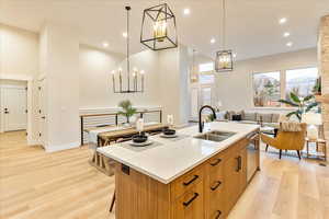 Kitchen with a center island with double sink, light  flooring, light stone counters, wood finish cabinets, and decorative light fixtures