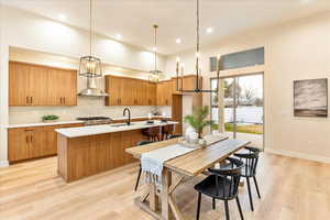 Kitchen featuring wood finish cabinets, hanging light fixtures, light wood-style floors, tasteful backsplash, and a high ceiling