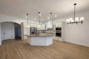 Kitchen featuring glass insert cabinets, arched walkways, white cabinetry, backsplash, and stainless steel appliances