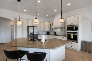 Kitchen with arched walkways, light wood-style floors, glass insert cabinets, a kitchen breakfast bar, and dark stone countertops