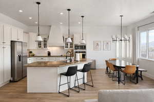Kitchen with glass insert cabinets, stainless steel appliances, light wood-style flooring, dark stone countertops, and a textured ceiling