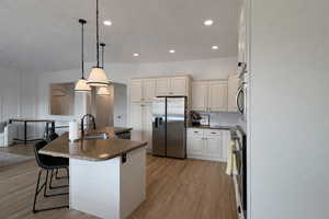 Kitchen featuring a breakfast bar, stainless steel appliances, light wood-style floors, a center island with sink, and hanging light fixtures
