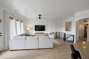 Living area featuring arched walkways, light wood-style floors, a ceiling fan, and a textured ceiling