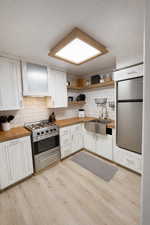 Kitchen featuring wood counters, white cabinets, open shelves, stainless steel appliances, and light wood-style floors