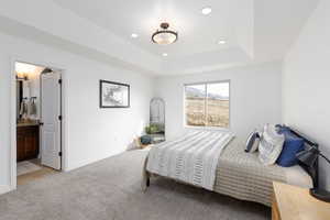 Bedroom featuring recessed lighting, light carpet, a tray ceiling, and ensuite bath