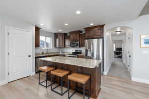 Kitchen with arched walkways, dark wood finish cabinets, a breakfast bar area, stainless steel appliances, and a center island