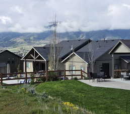 Rear view of house featuring a mountain view, roof with shingles, a patio, and a lawn