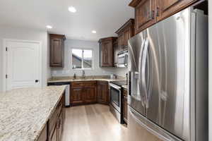 Kitchen featuring stainless steel appliances, dark wood finish cabinets, light wood-style floors, light stone counters, and recessed lighting