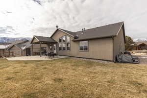 Rear view of property with a patio area, a yard, a shingled roof, and stucco siding